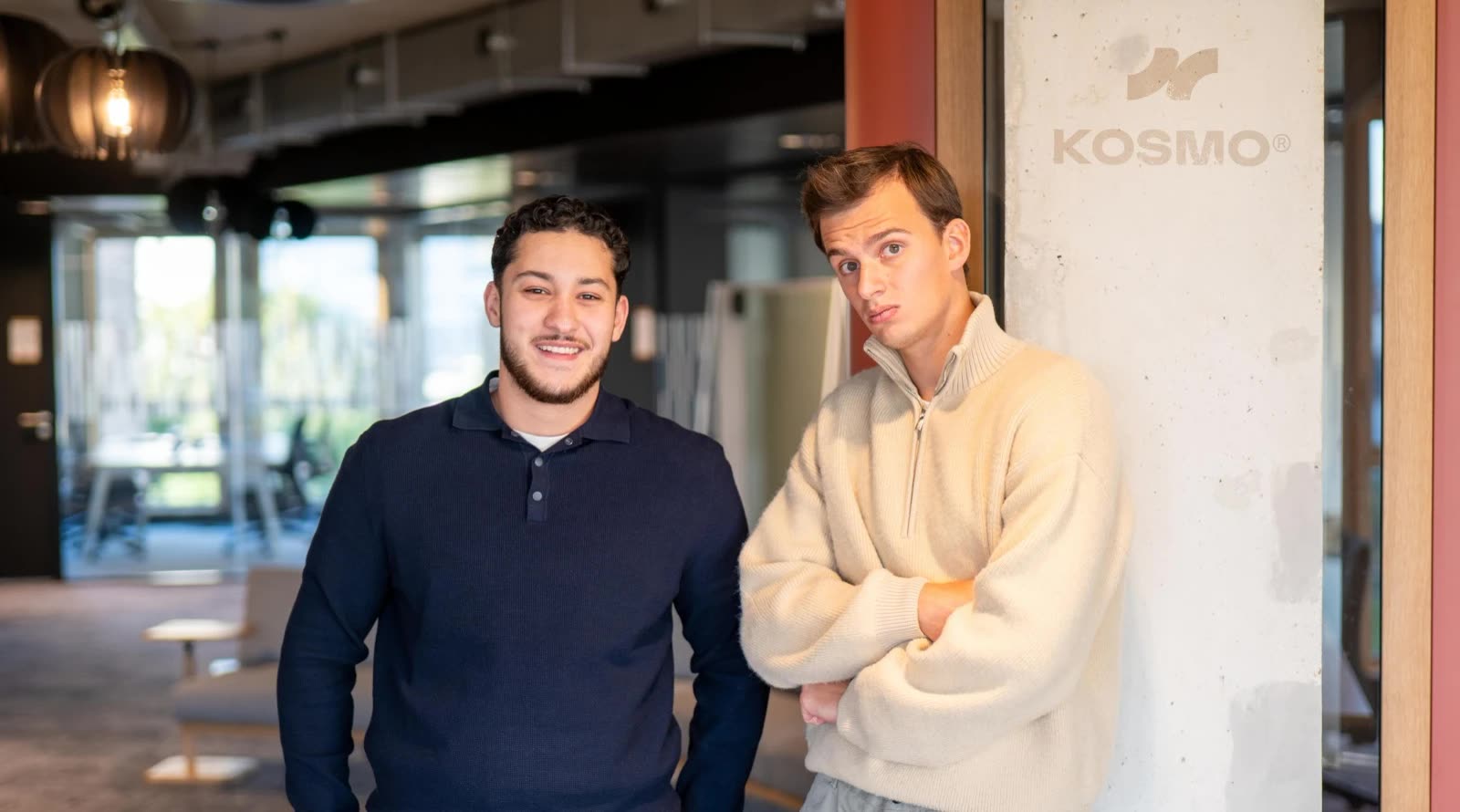 Mehdi Benkaci en Eugène Roux op het kantoor van KOSMO®, voor het KOSMO®-logo op een betonnen pilaar