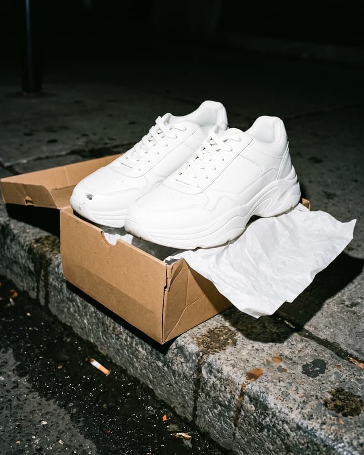 New white sneakers in their box on a city curb at night