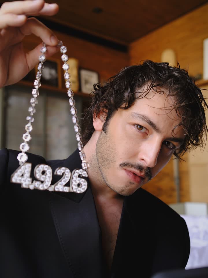 Un membre du casting tenant le collier 4.9.26 face à l’objectif