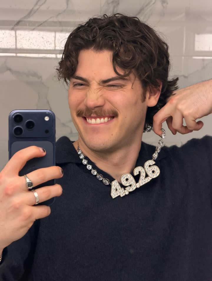 Un membre du casting en selfie miroir, le collier 4.9.26 au cou