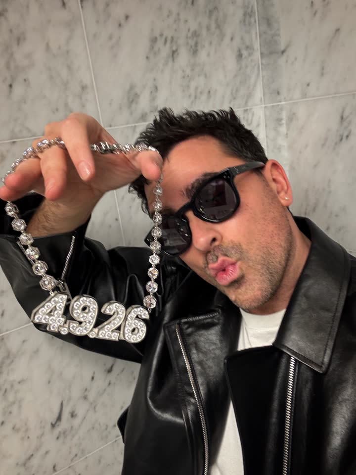 Dan Levy en lunettes de soleil et veste en cuir tenant le collier 4.9.26