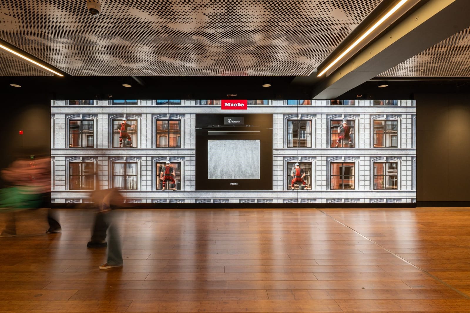 Miele HydroClean DOOH campaign on the Business Wall at Westfield Les 4 Temps: a CGI building facade with workers at the windows and the HydroClean oven in the middle