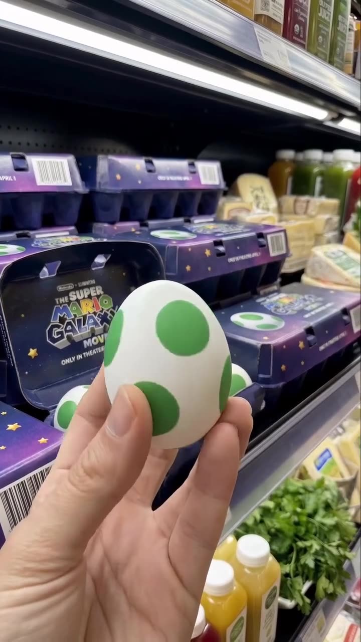 Un œuf Yoshi tenu en l’air, des boîtes empilées sur le rayon derrière