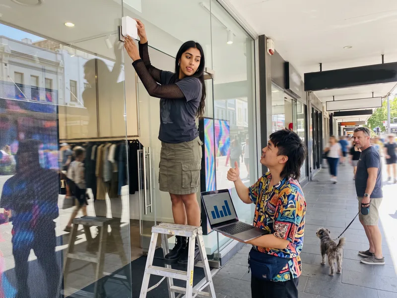 A people counter is fixed above a boutique entrance while a colleague checks the data